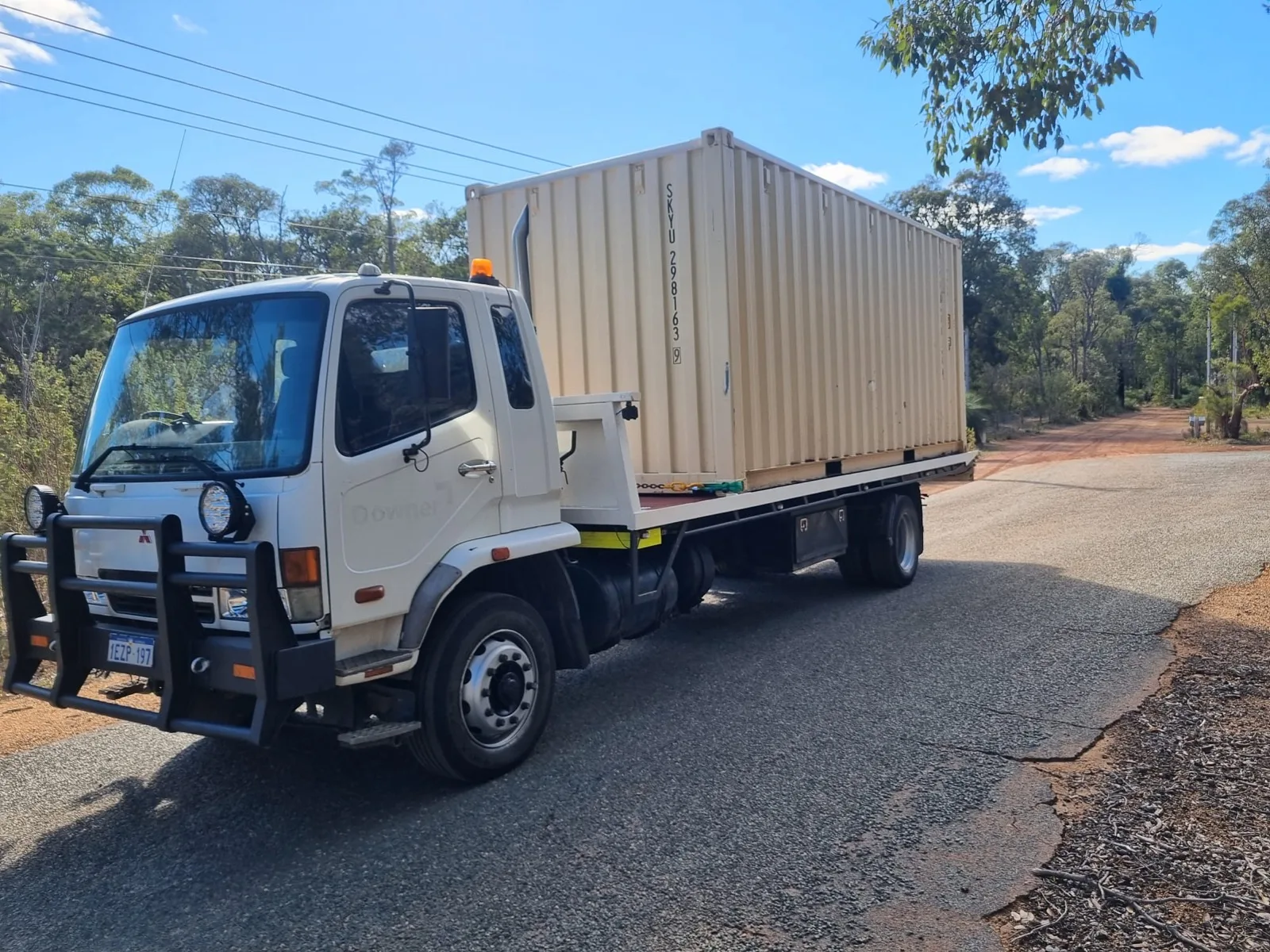 Australian Premium Logistics tilt tray carrying a shipping container on a regional Western Australian road